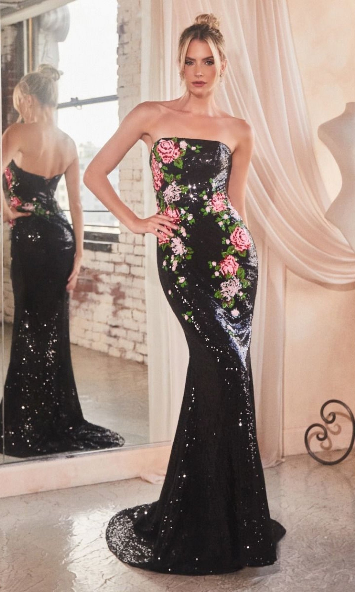 A woman wearing the Strapless Long Sequin Floral Formal Dress CD811—floor-length, black sequins with pink floral print—stands before a mirror in a well-lit room with draped curtains.